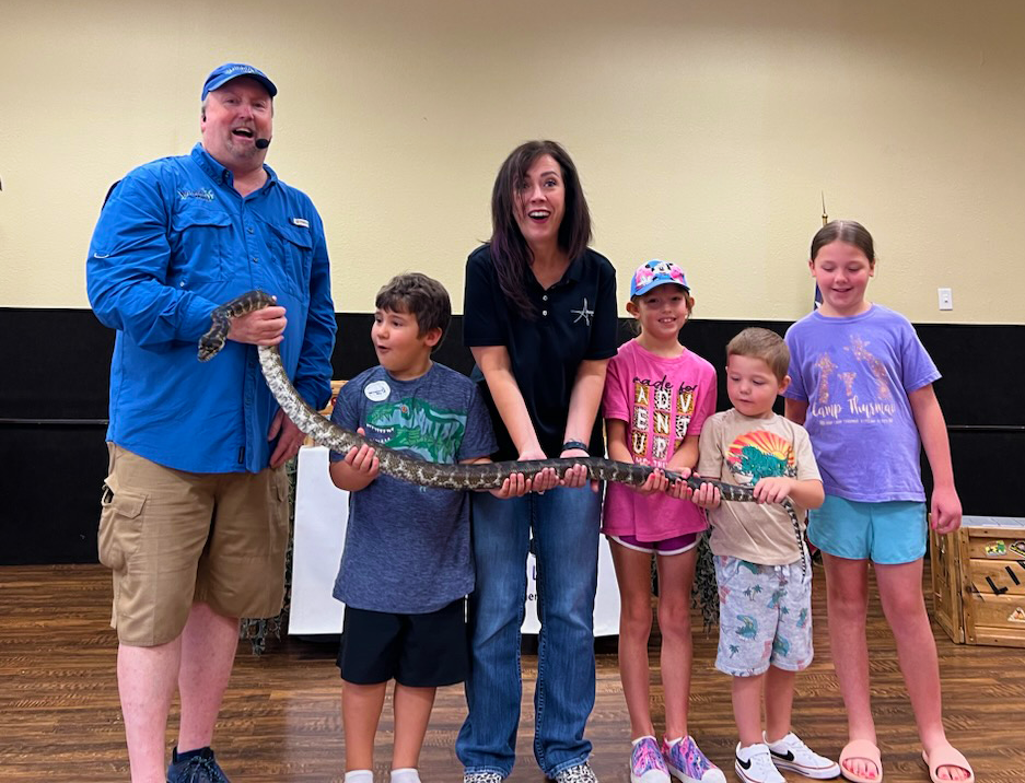 Line of adults and children holding a big snake
